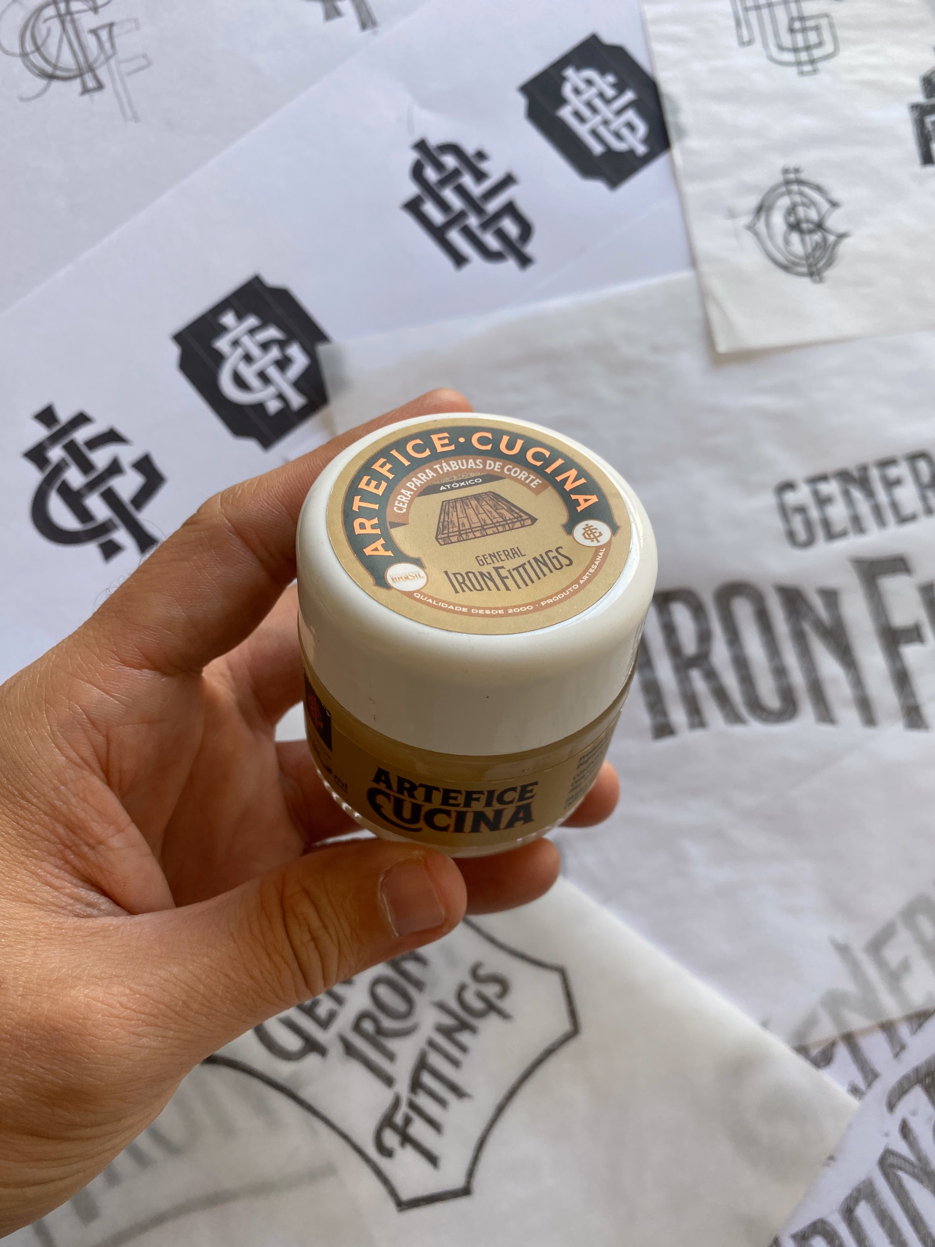 Artefice Cucina cutting-board wax by General Iron Fittings held over papers printed with the GIF monogram